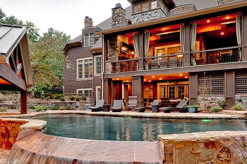 Backyard patio & pool design behind a large two-story home with brown siding.