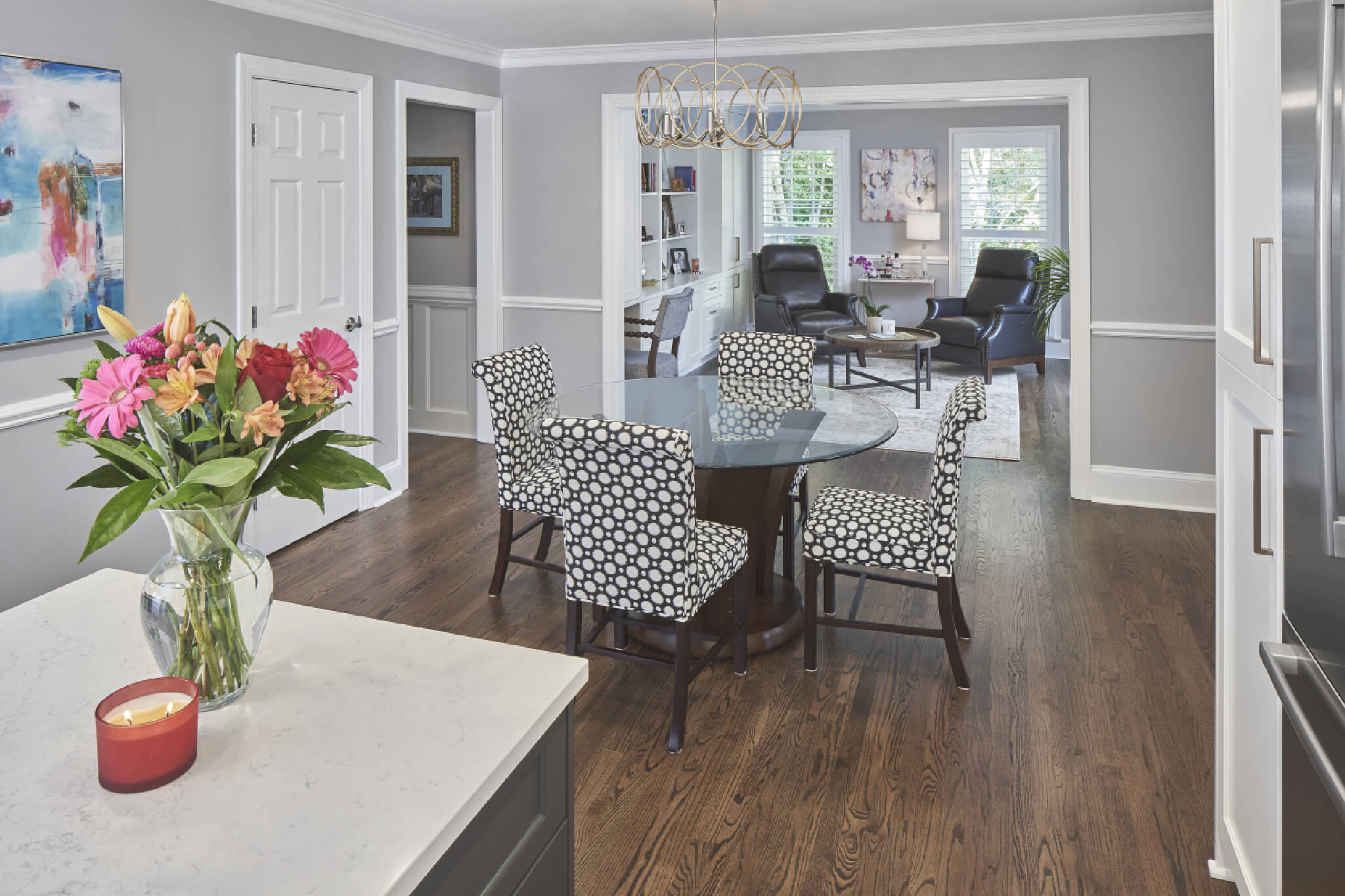 Open concept kitchen with wood floors and round glass dining room table with black & white upholstered dining chairs. Light gray walls and white trim.