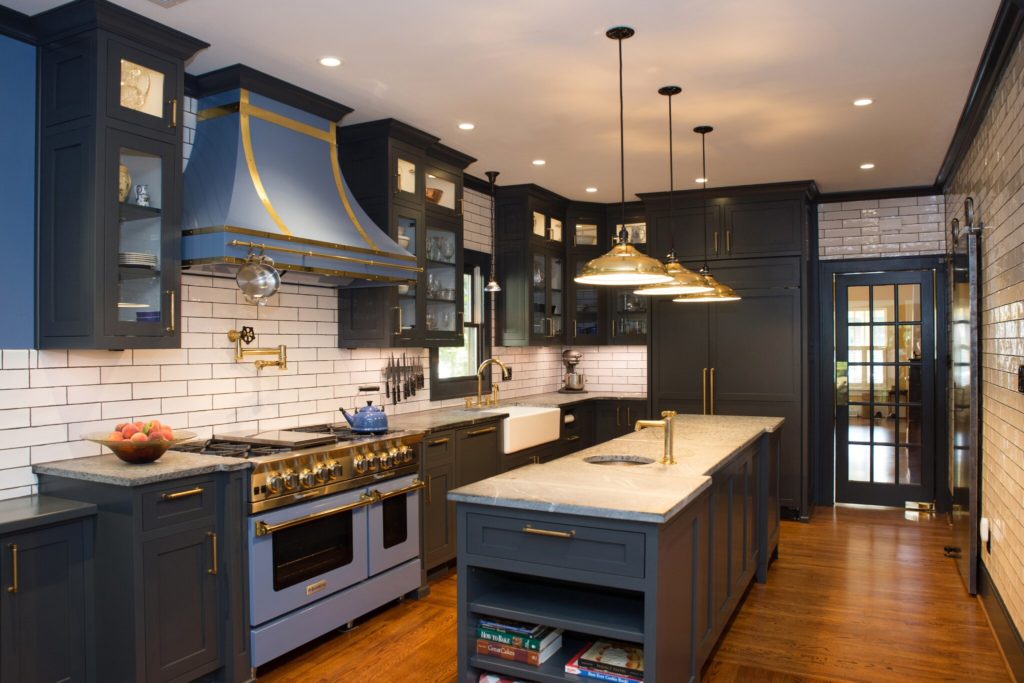 Remodeled kitchen with black cabinets, stone countertops, large island, gold fixtures, pendant lighting, and blue accents.