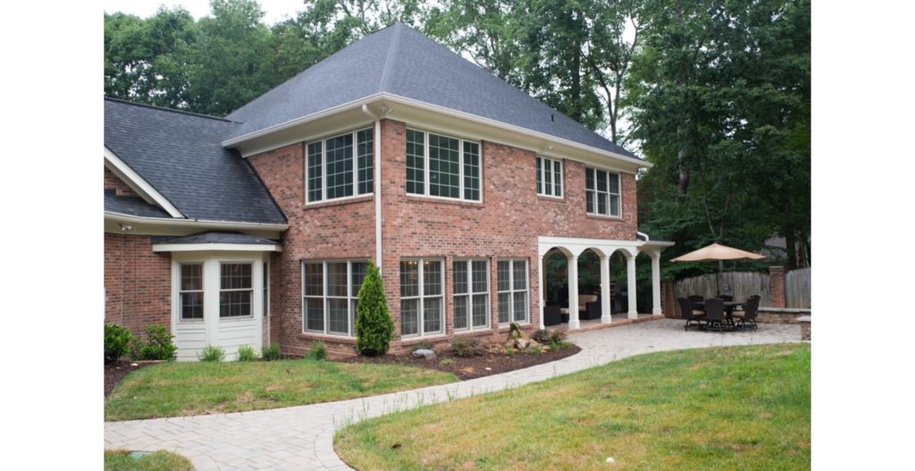 Exterior of large brick home addition with floor-to-ceiling windows and covered porch with white arches and columns