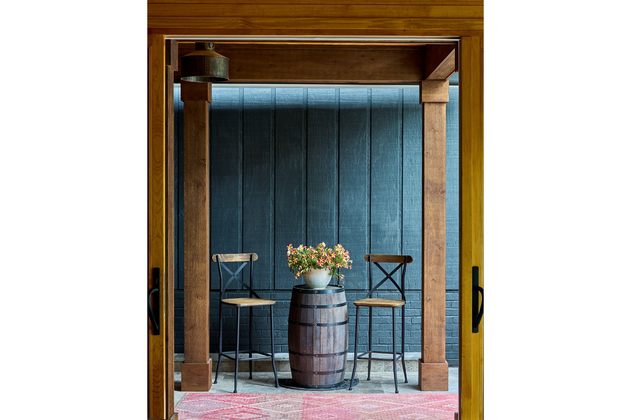 small outdoor seating space of home two tall bar stools barrell between them with flower bouquet