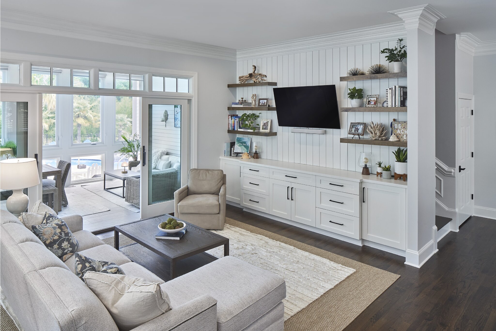 Light and bright coastal living room with white shiplap walls, custom built-in media storage, and large glass sliding doors into sunroom