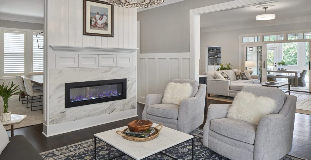 Remodeled living area with built-in fireplace, white molded wainscoting, gray couches, and a table.