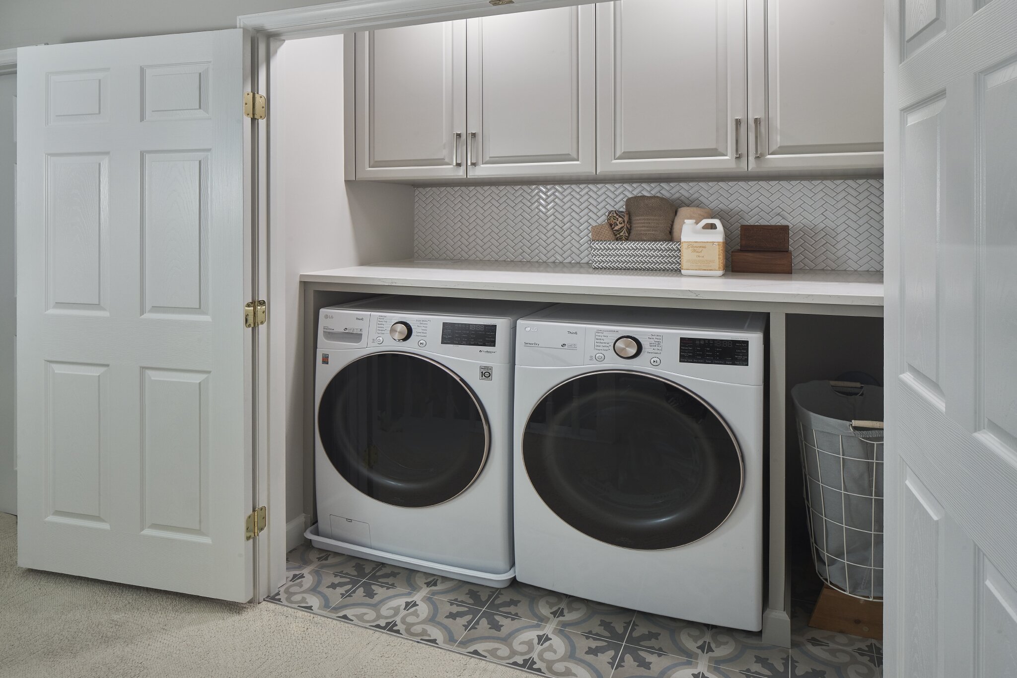 Renovated laundry room tucked behind two large french doors, with countertop and overhead cabinetry