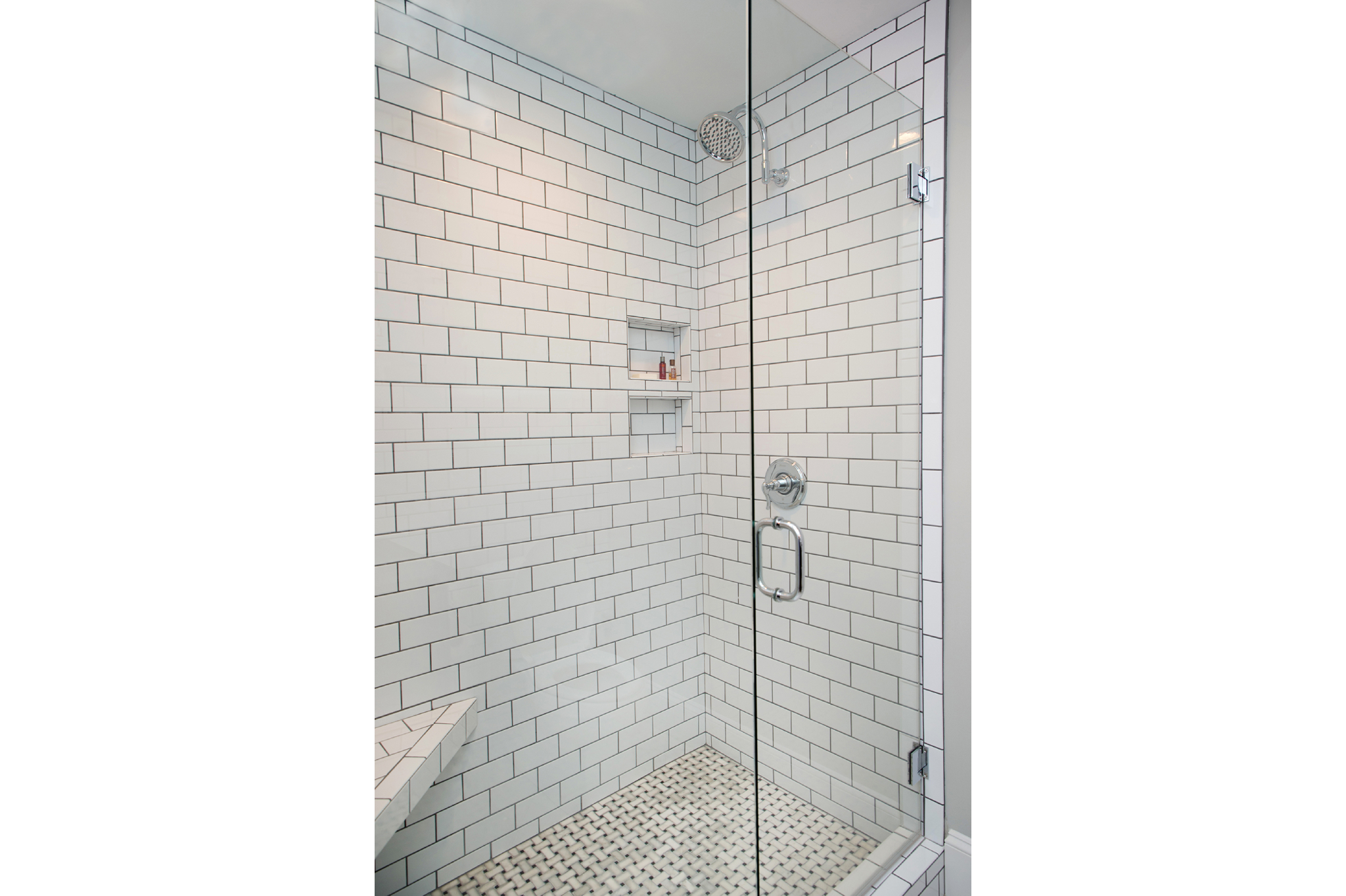 White subway-tiled shower walls with dark grout and contrasting woven-patterned tile floor