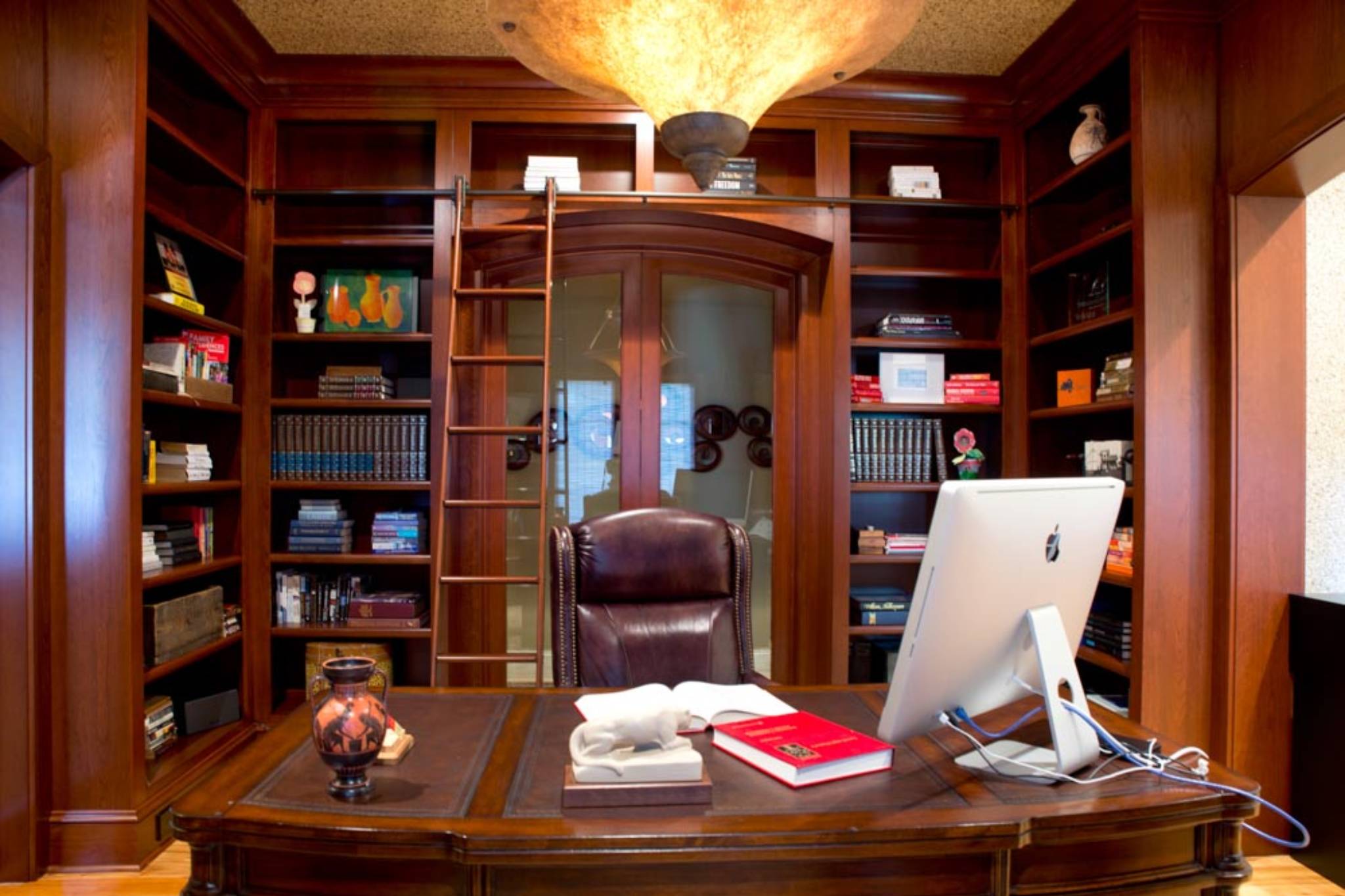 Sophisticated cherry-wrapped home library with built-in bookshelves and custom elliptical glass sliding doors