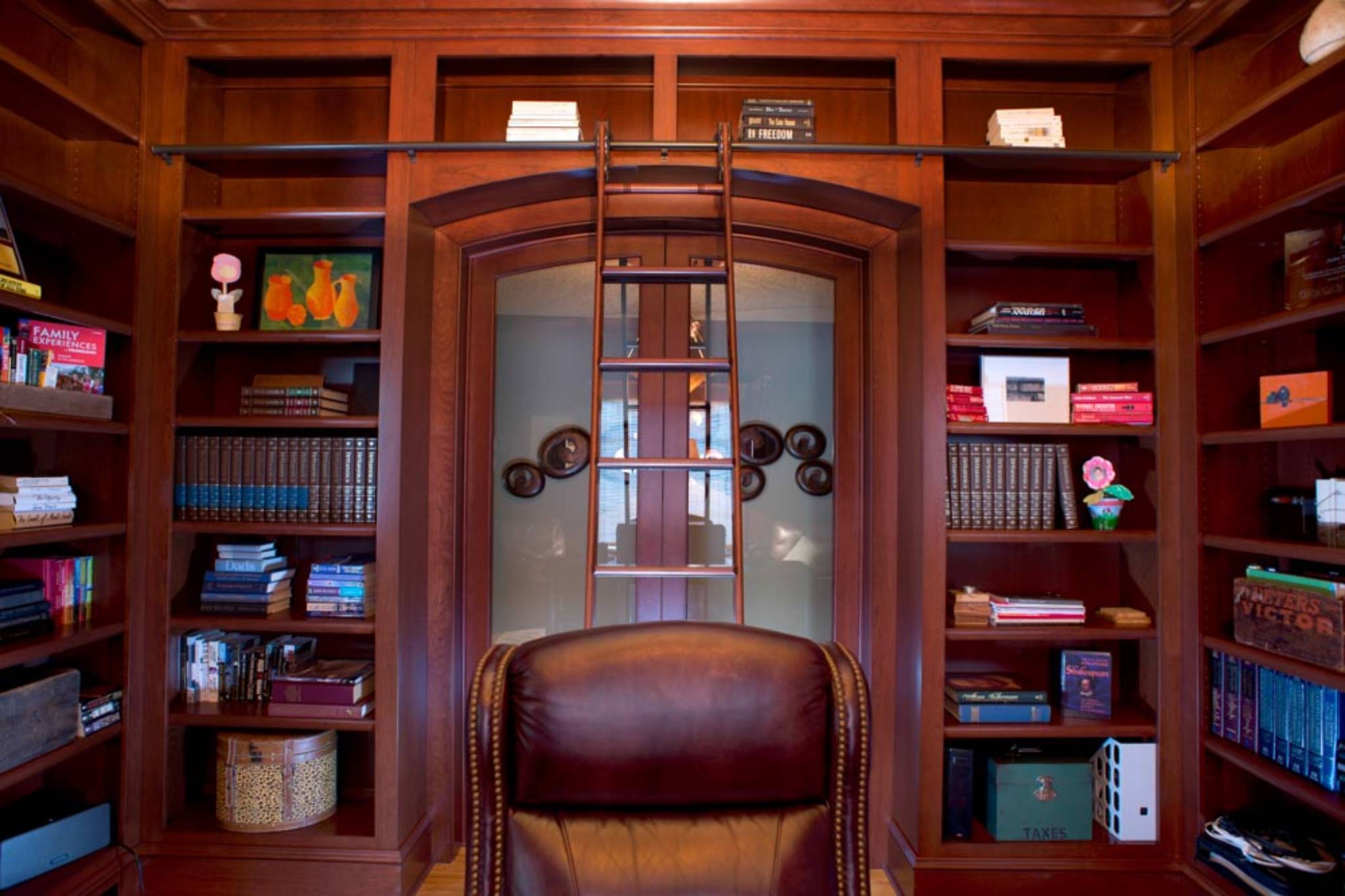 Sophisticated cherry-wrapped home library with built-in bookshelves and custom elliptical glass sliding doors