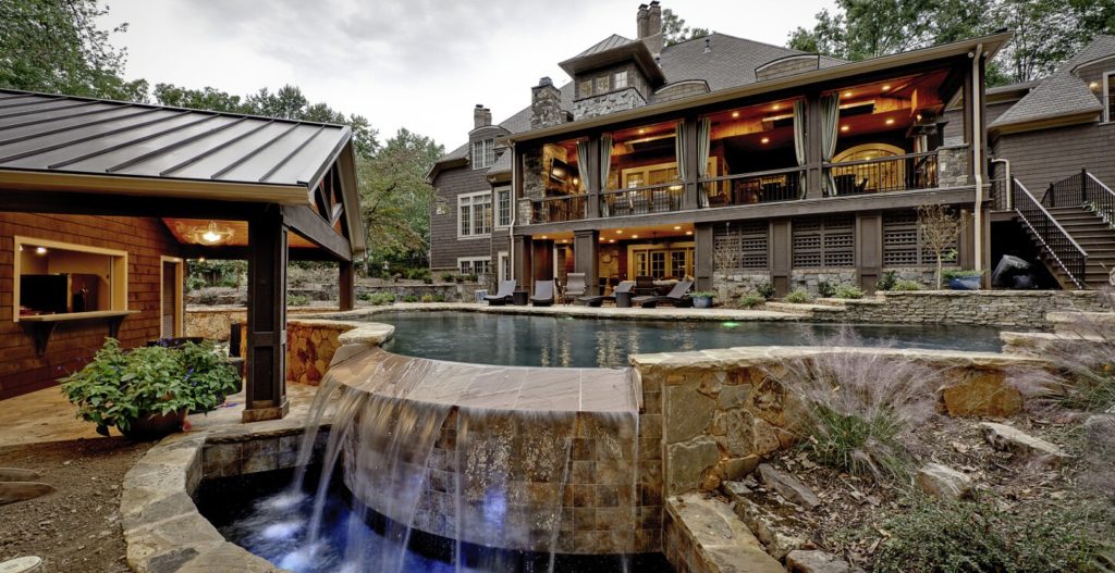 Porch addition on large stone house with infinity pool and waterfall feature.