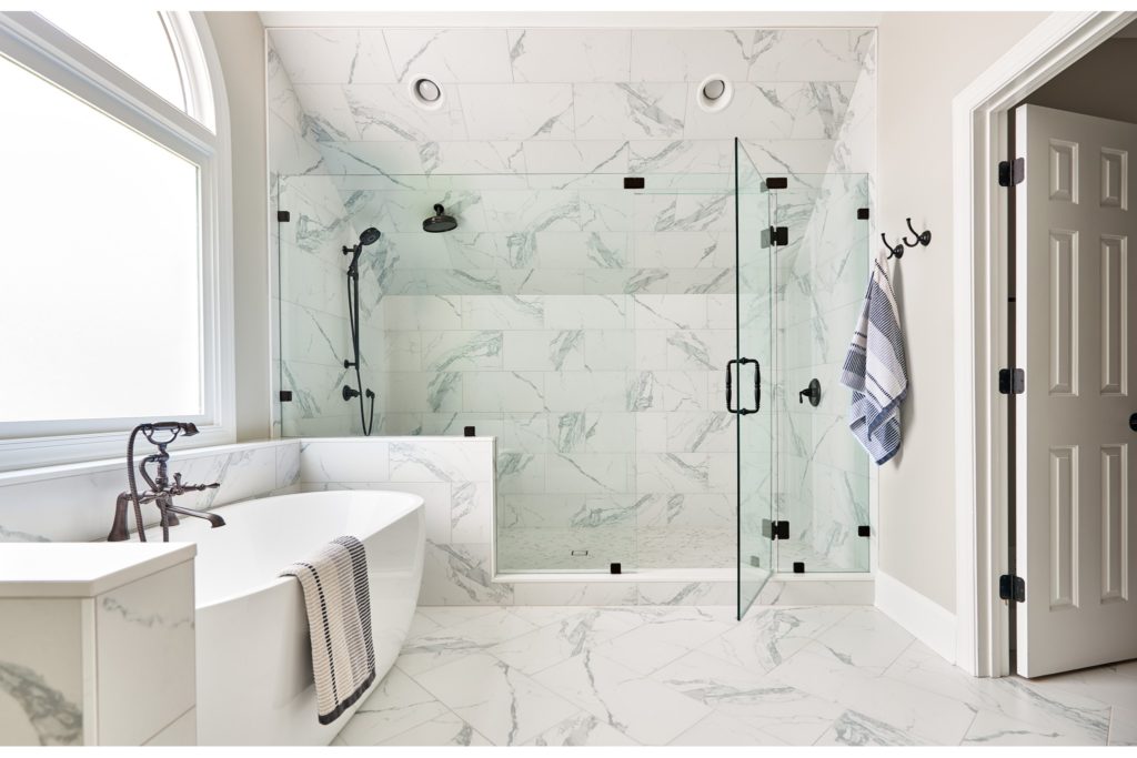 Bright, open, clean bathroom renovation with floor-to-ceiling marble tile, freestanding tub, and glass shower.