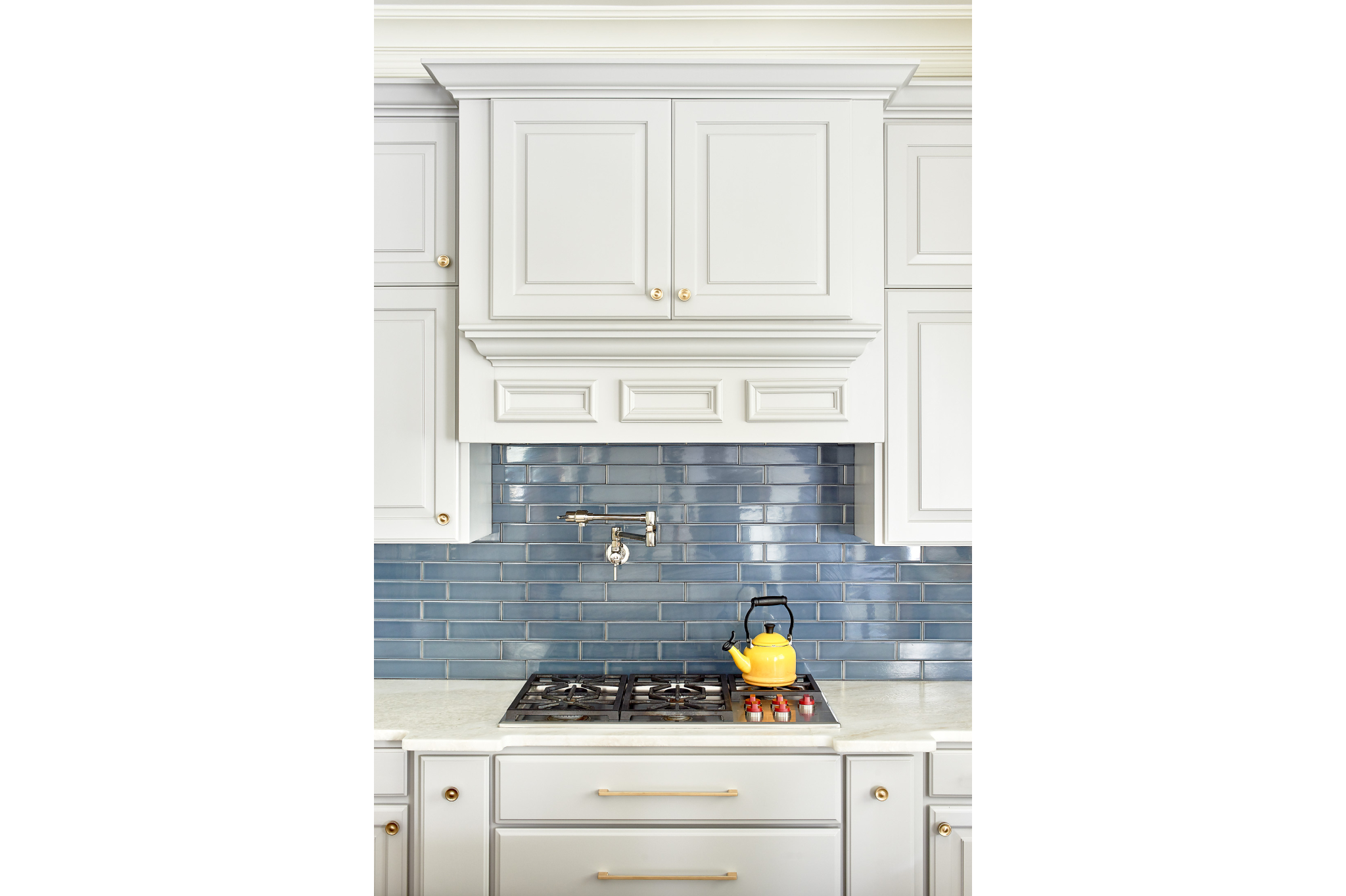 Upgraded kitchen stovetop with custom vent hood, dark blue subway tile, and satin brass accents