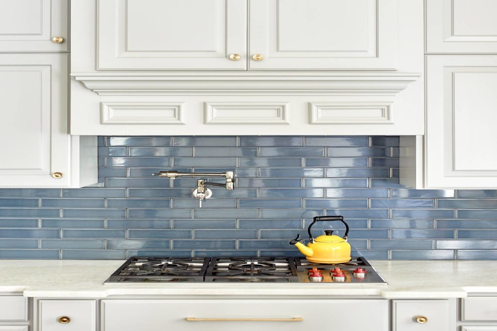 Close-up of white kitchen cabinetry with a blue tile backsplash over a stove.