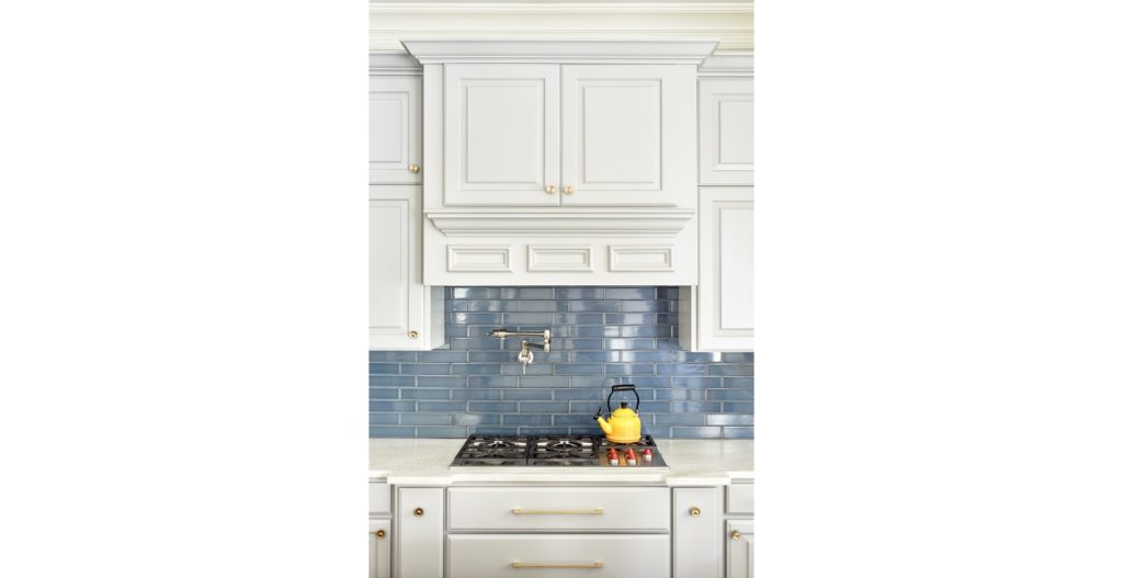 Remodeled kitchen with traditional style white cabinets and blue subway tile backsplash behind gas stove.