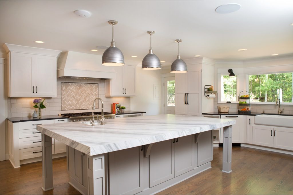 Kitchen renovation large marble island with storage and chrome pendant lights, white cabinets, wood floors.