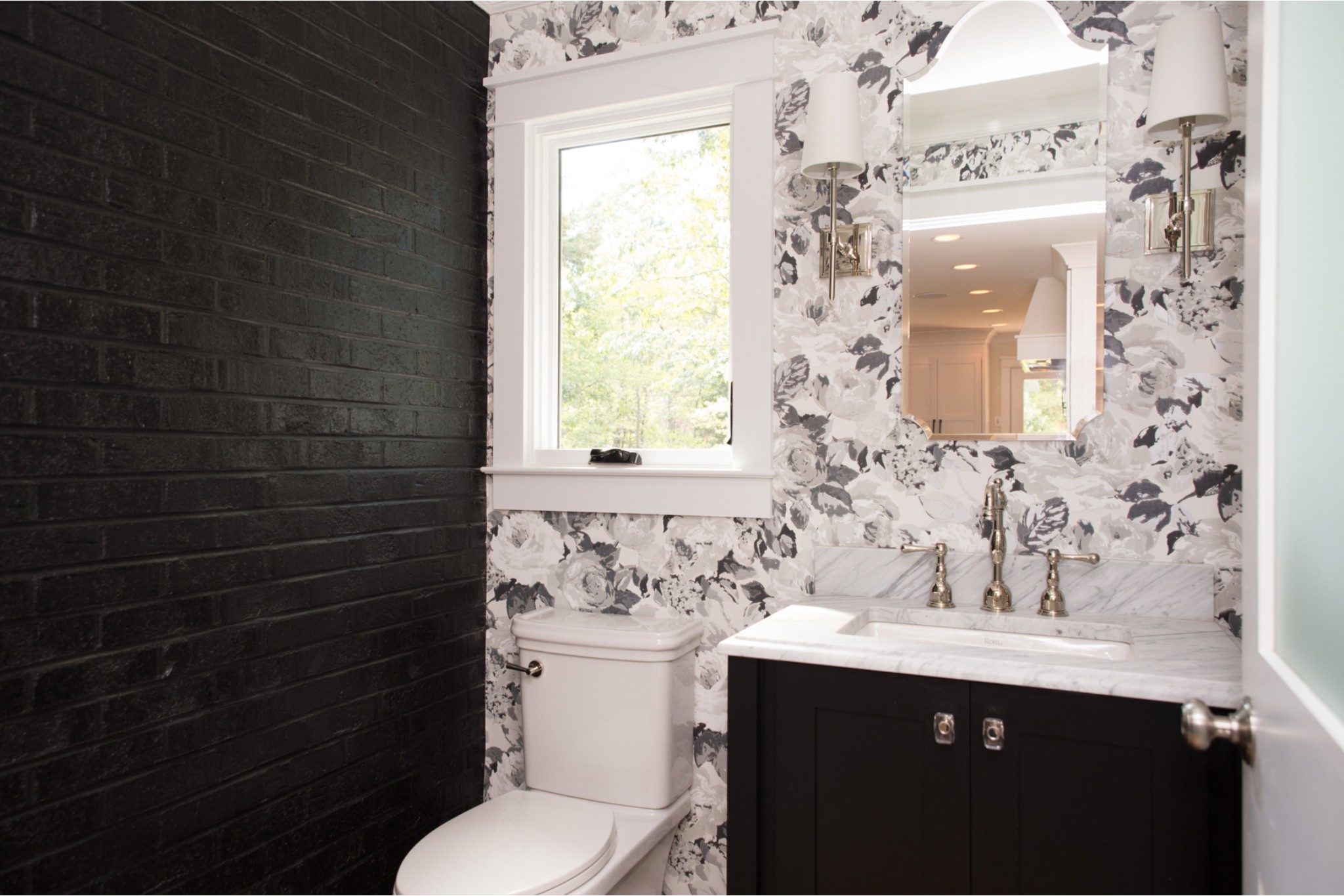 bathroom removal black brick wall beside white, grey and black flower wallpaper behind toilet