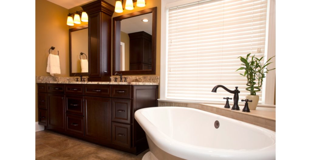 Remodeled bathroom with double vanity, large picture window, and corner free-standing tub with ledge