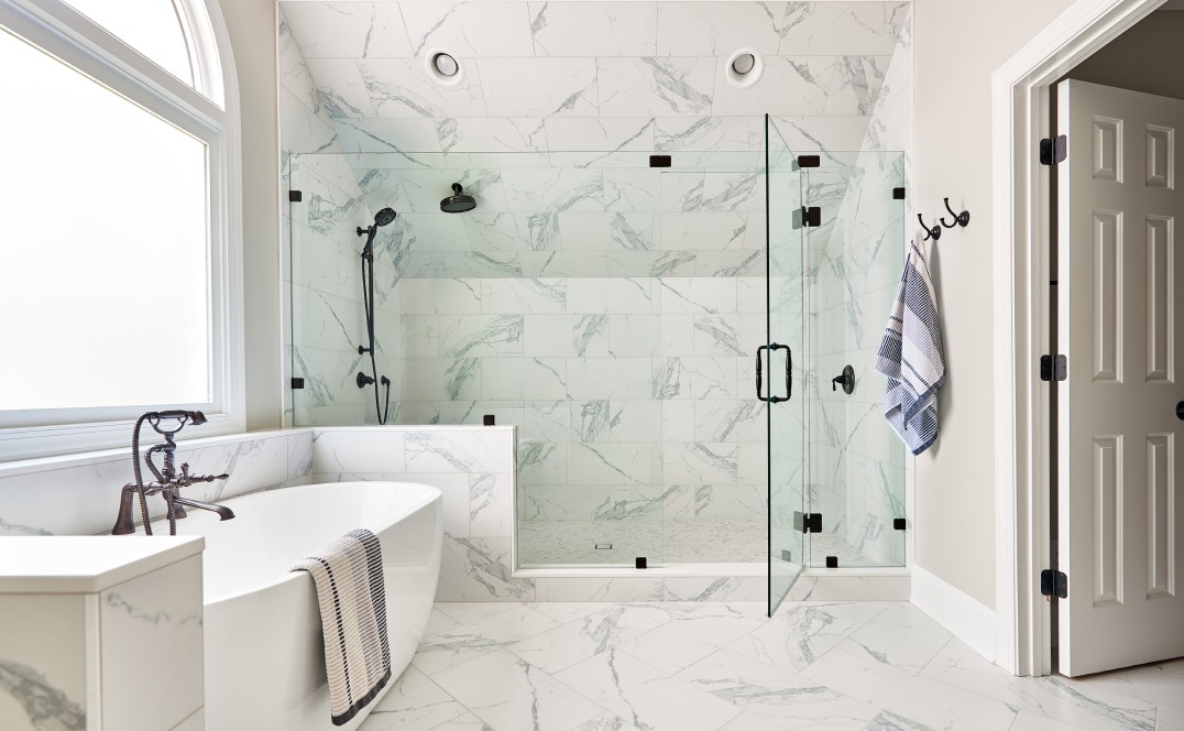 newly remodeled bathroom with white marble tile, a porcelain bathtub and a frameless glass shower