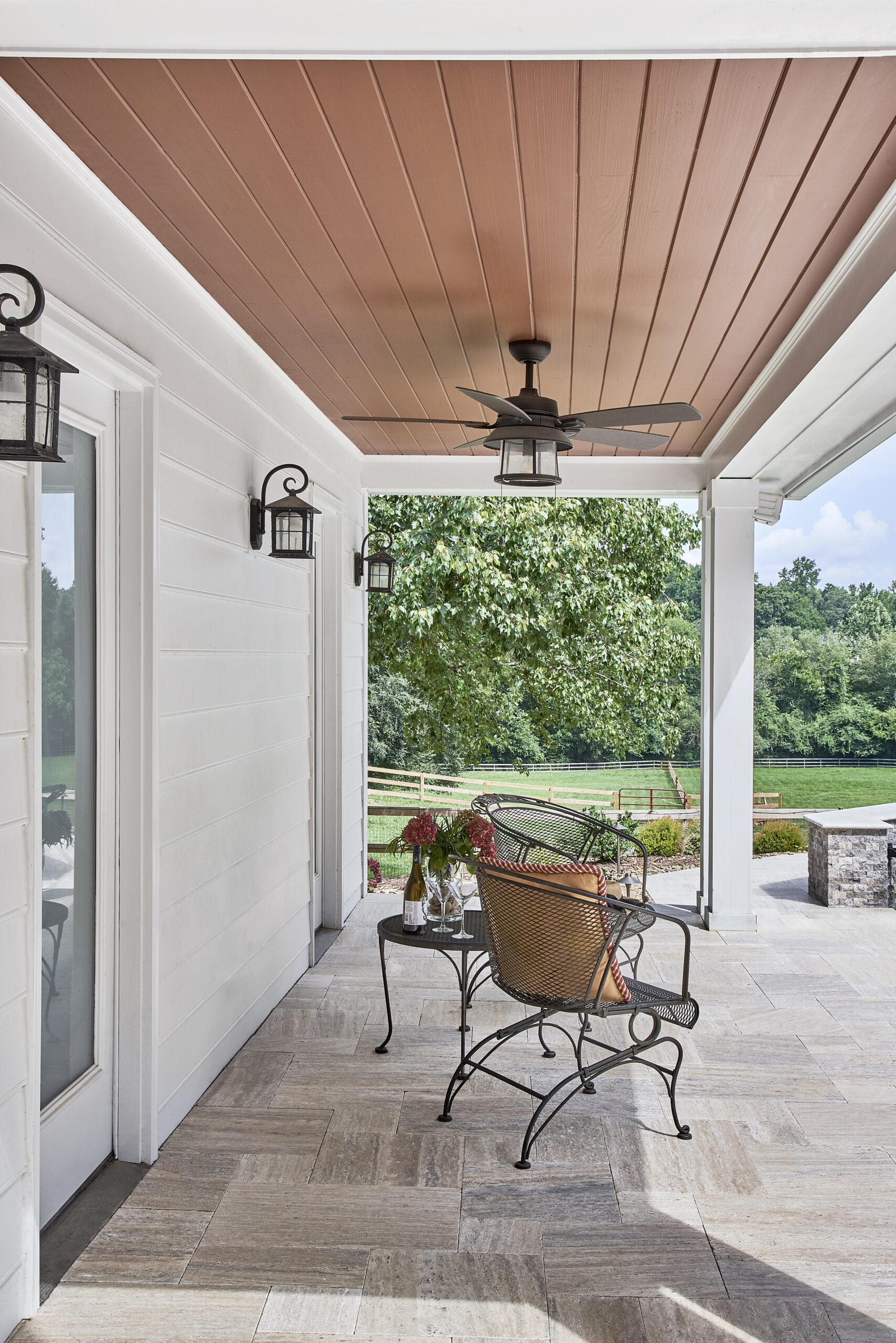 Shaded porch with wood paneled ceiling and fan.