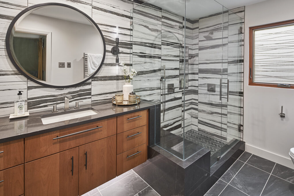 Bathroom remodel with black-striped white marble tile wall, glass-enclosed shower, woodgrain vanity with dark stone countertop, black tile floors.