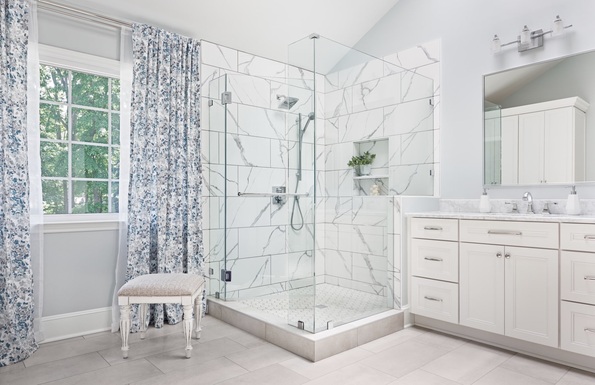 Bathroom remodel with glass-enclosed shower and white vanity. White tile floors and white marble tiles in shower.