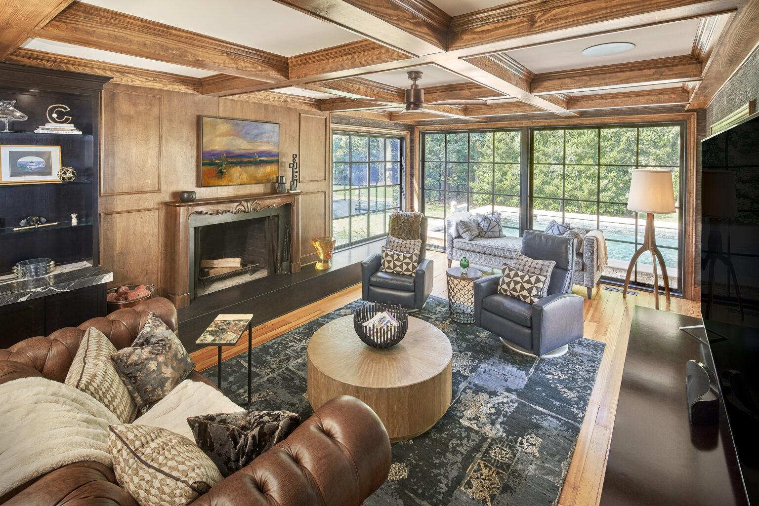 Luxurious sunroom addition with coffered ceilings, wood floors, large floor-to-ceiling black framed windows with grids on far wall, and a fireplace.