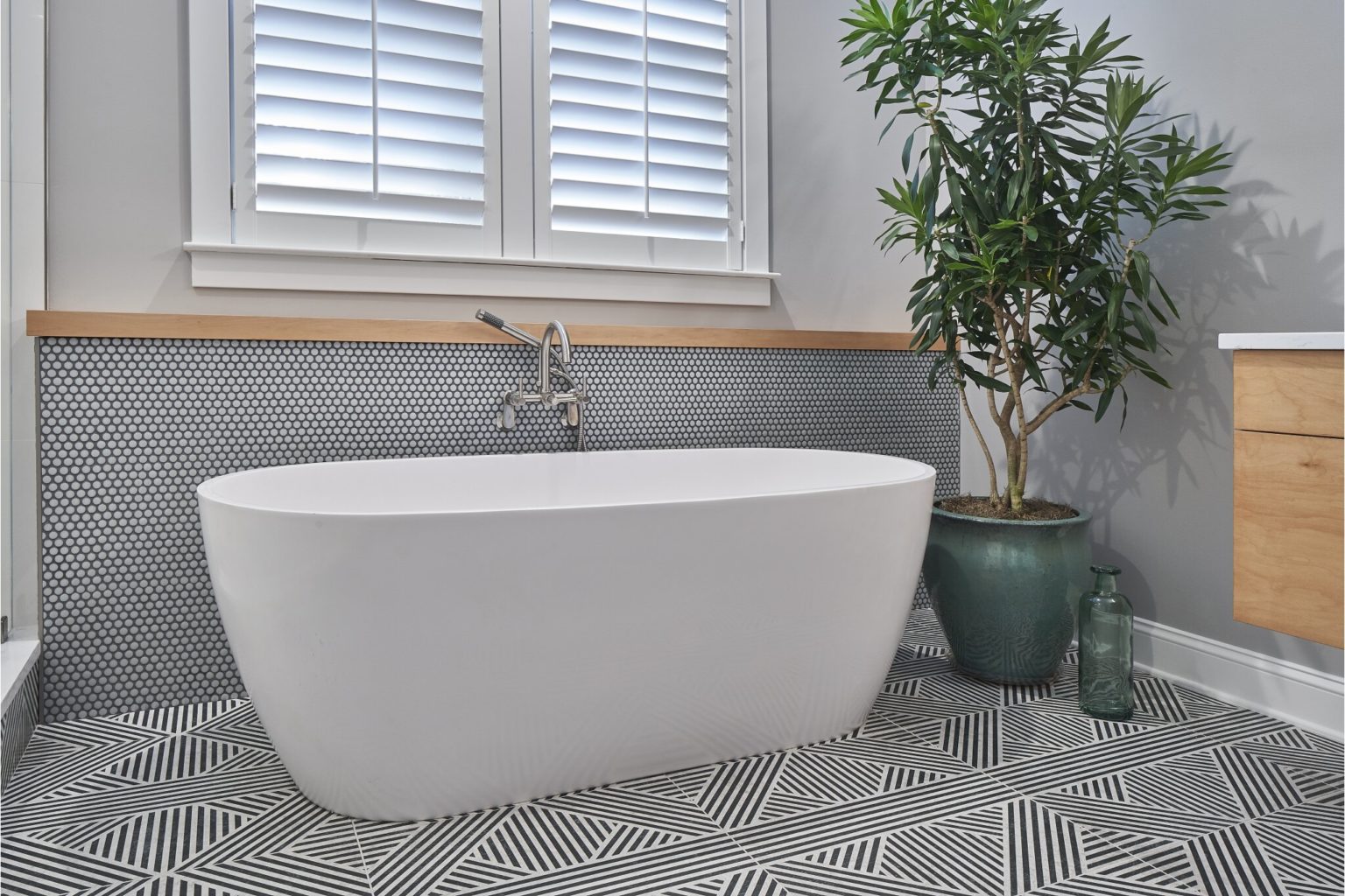 White free-standing tub in a bathroom with black and white stripe-patterned floor tiles.