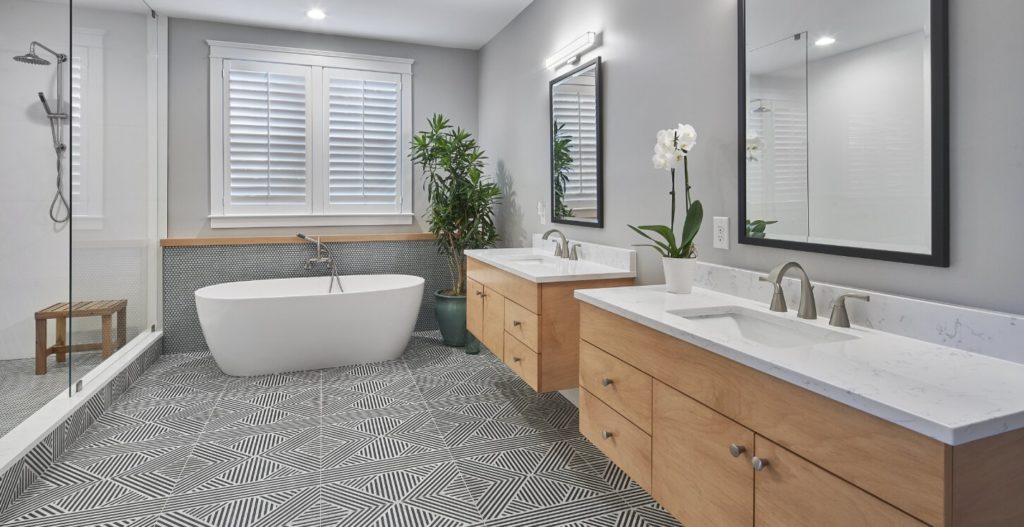 Remodeled bathroom with two vanities, geometric-patterned tile floor, and a stand-alone tub.