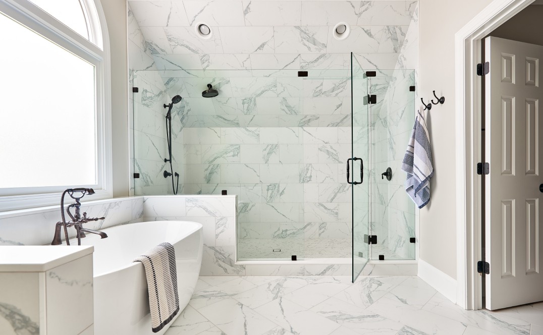 Newly remodeled bathroom with white marble tile, a porcelain bathtub, and a frameless glass shower