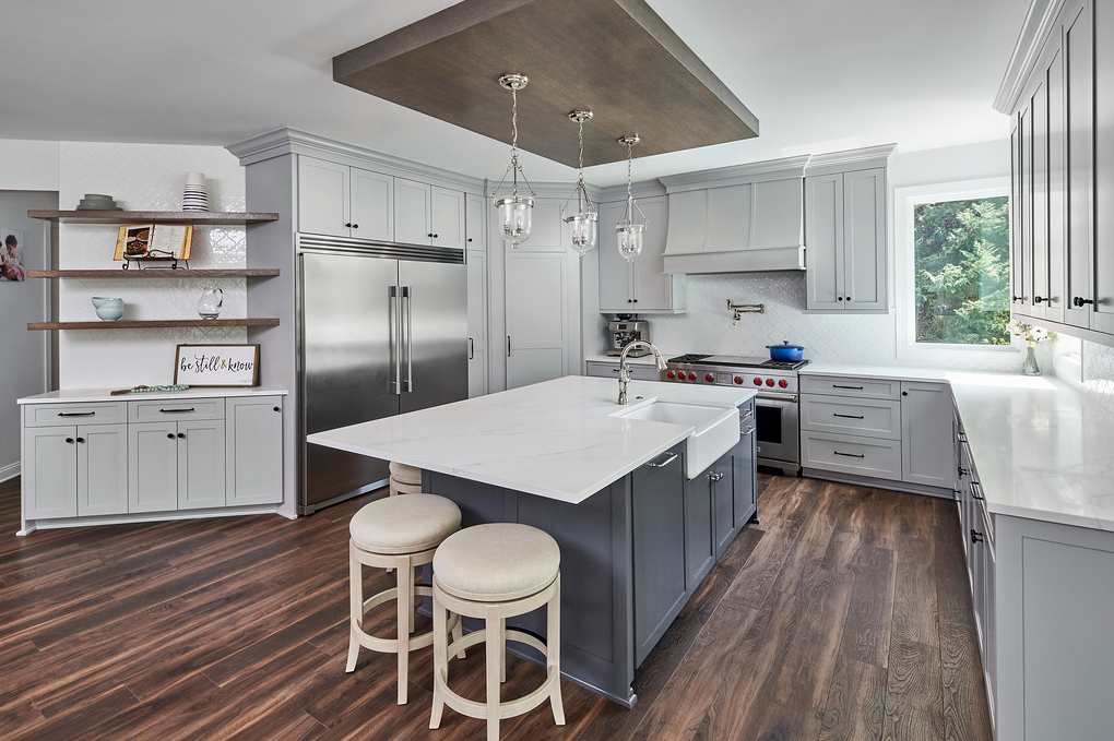 Remodeled kitchen with wood floors, pale gray cabinets, white walls, dark gray/blue cabinets for the center island, white stone countertops.
