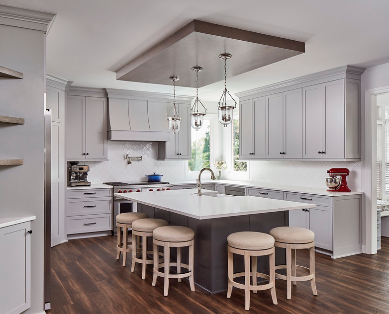 Remodeled kitchen with wood floors, white cabinets, large island in center with white stone countertop and stool seating around two sides.