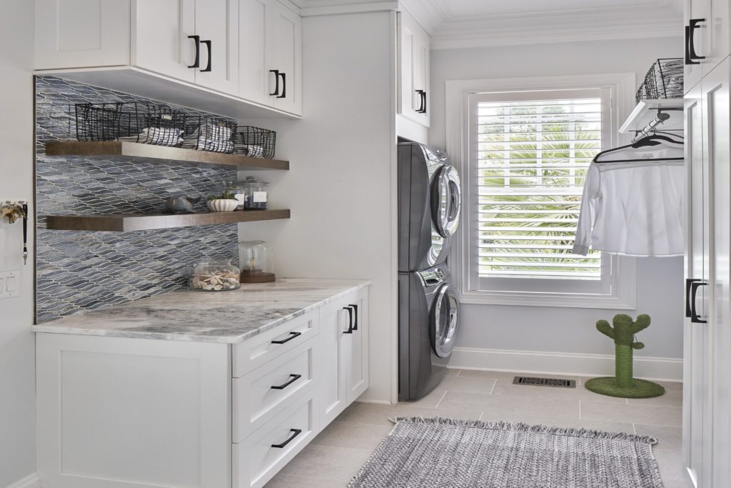Laundry room with white cabinets and gray backsplash.