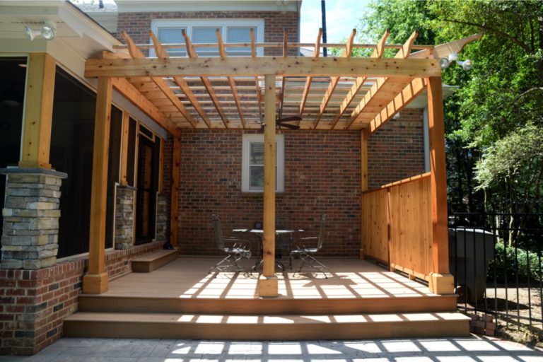 Wooden porch addition with a pergola and dining table, alongside a brick home.