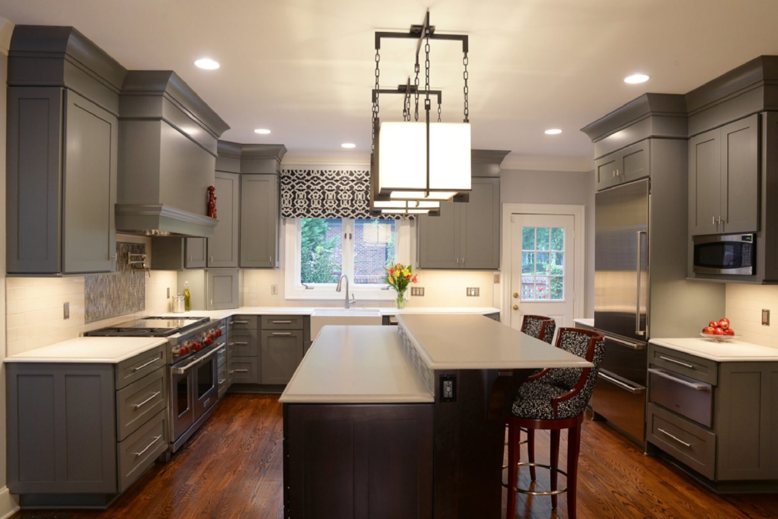 U-shaped kitchen with wood floors, gray cabinets, white stone countertop, and island in the middle with stool seating.