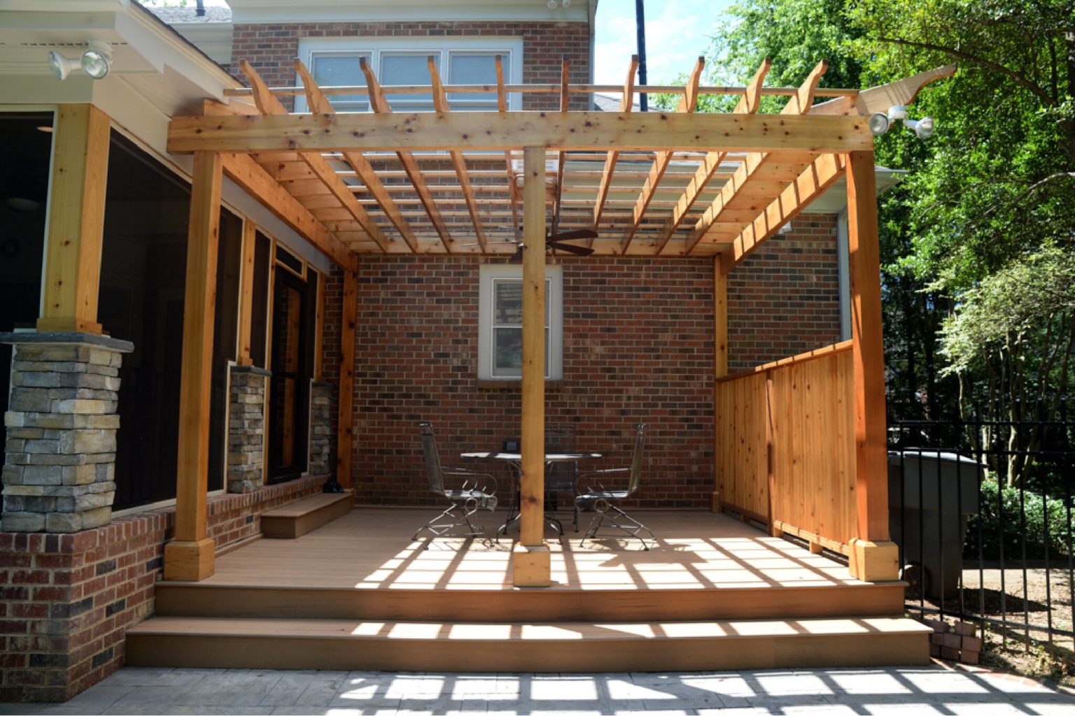Wood patio off the back of a brick home, with wood pergola over it.