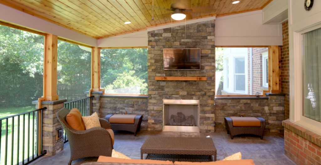 Custom home addition of enclosed patio with couch and TV over stone fireplace. Wood trim and wood-beams ceiling.
