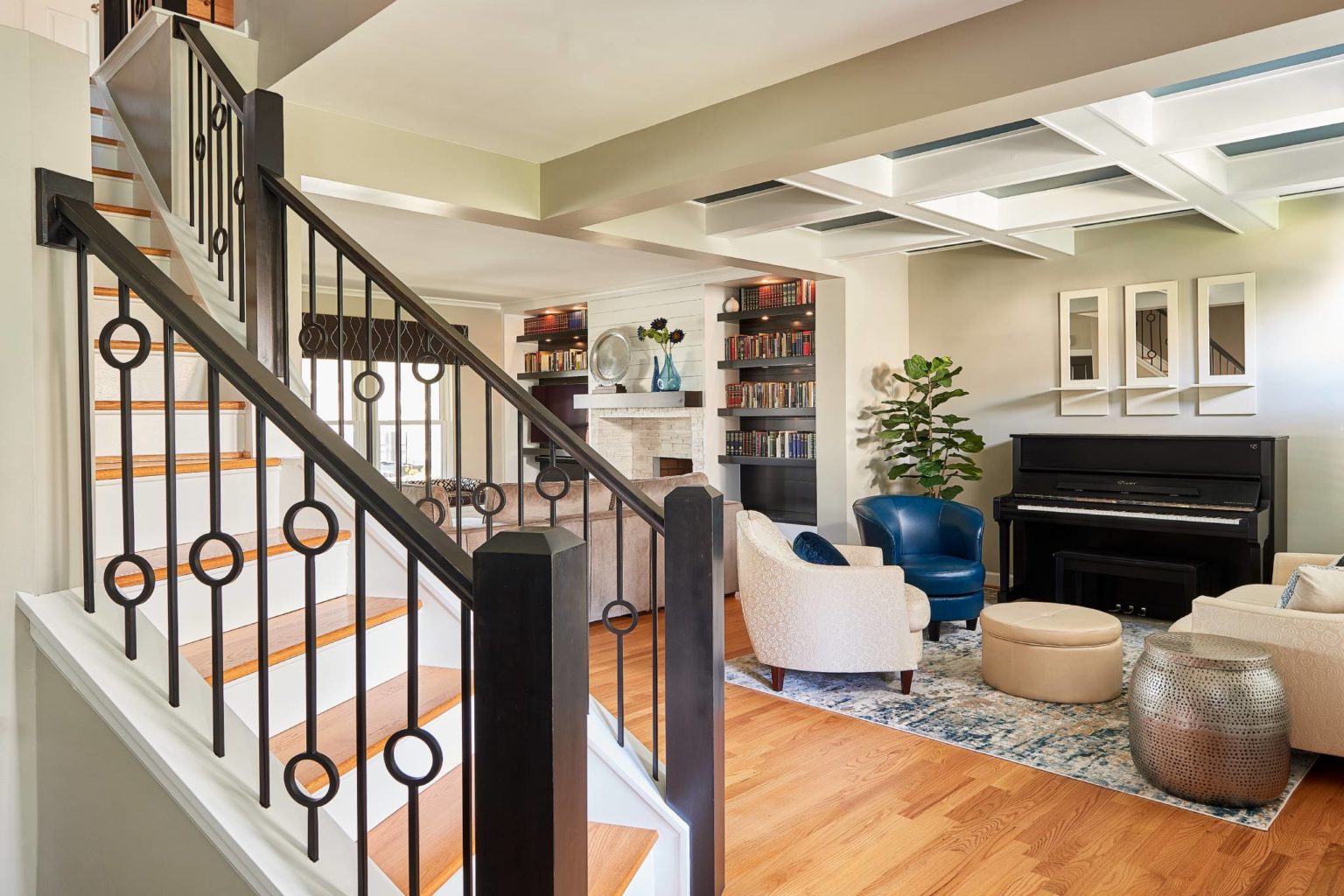 Split living room remodel with light hardwood flooring, curved staircase, off-white walls, and unique modern ceiling style.