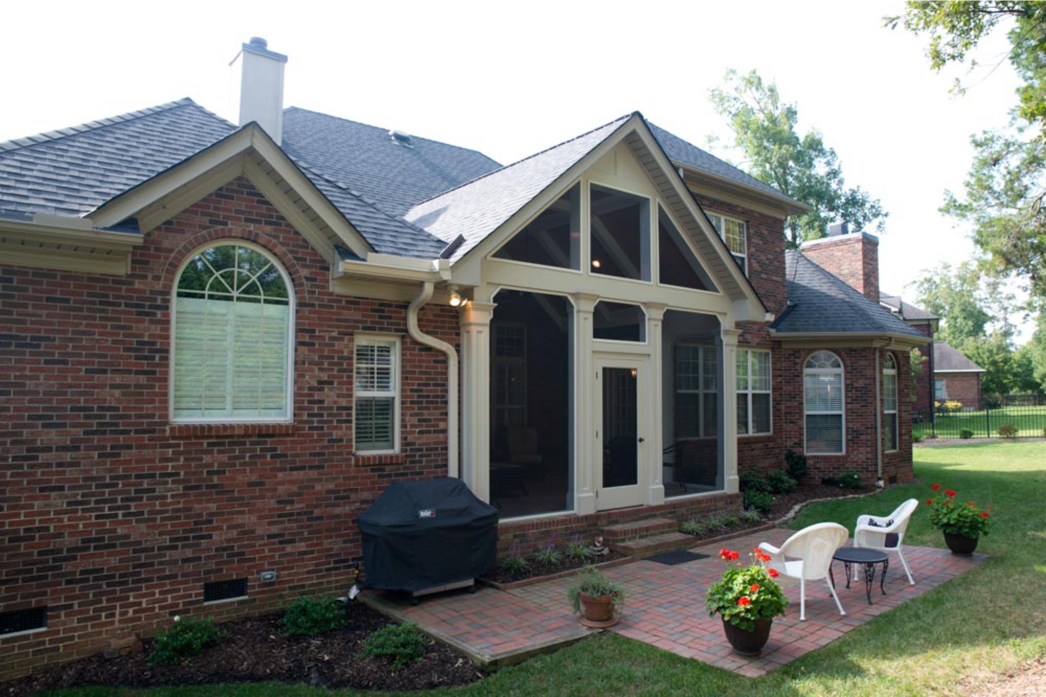 Brick home with elegant four seasons porch addition with thick off-white trim and built-in columns