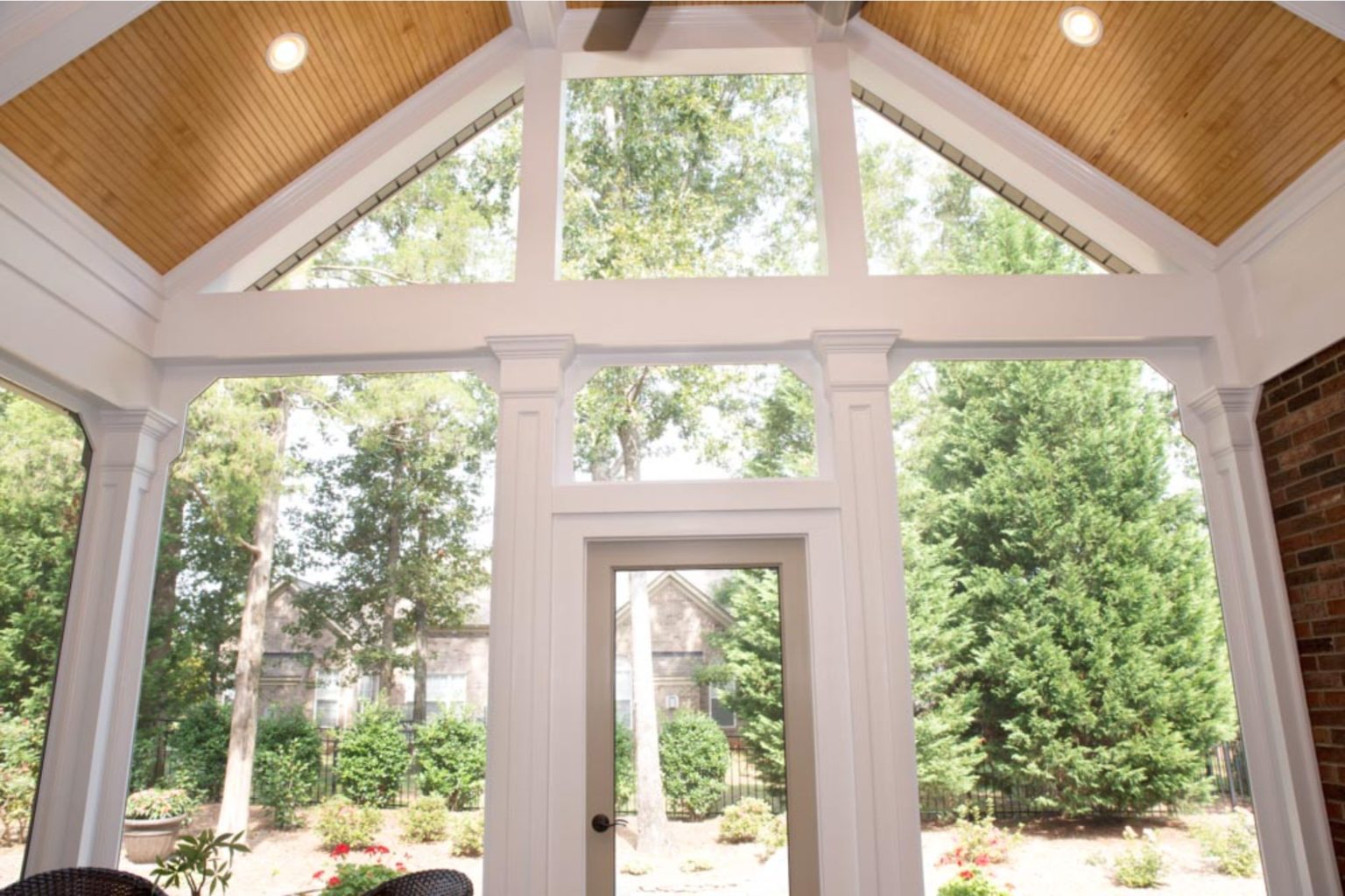 Sunroom with tall light wood beam ceiling, large windows, and recessed lighting. Door leading to garden area outside.