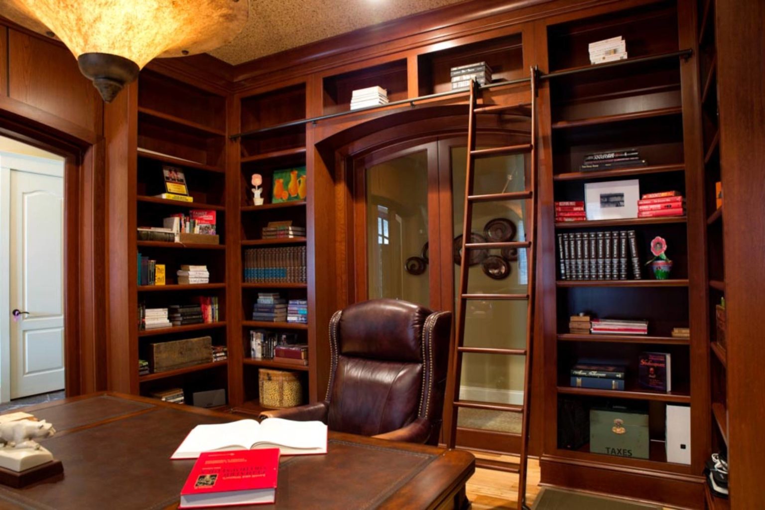 Sophisticated cherry-wrapped home library with built-in bookshelves and custom elliptical glass sliding doors