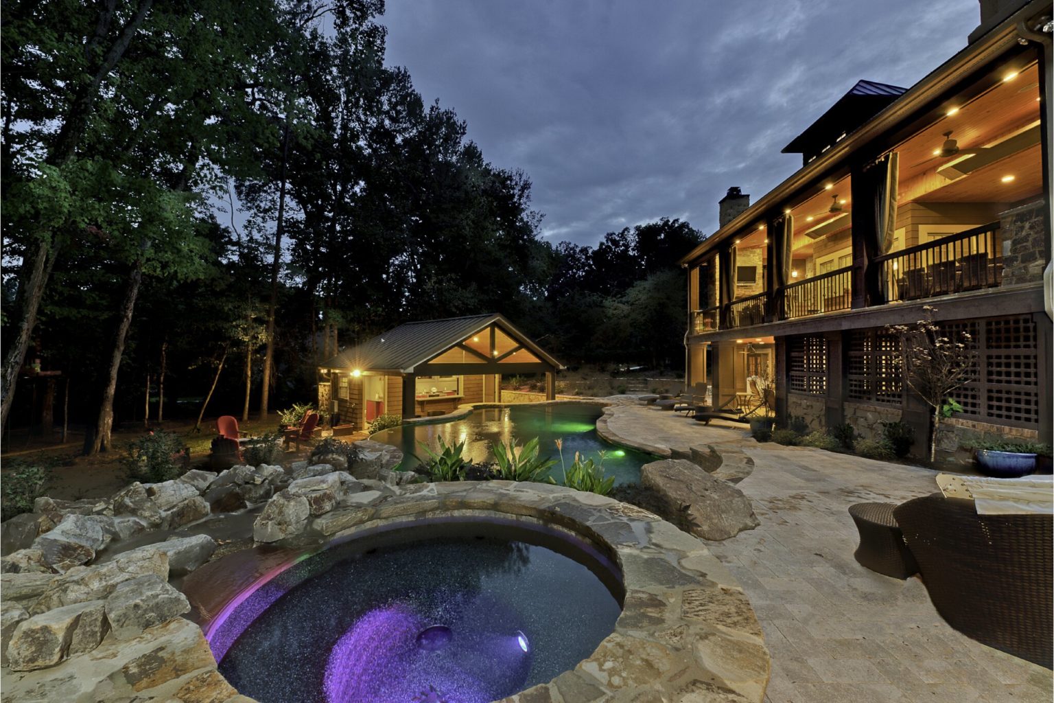 Stone-surrounded in-ground pool area behind a large house at night.