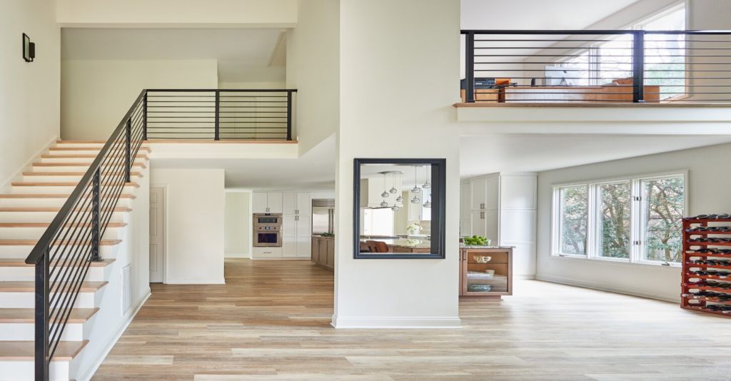 Whole-home open-concept remodel with light wood floors, white walls, stairway, and loft with black railings.