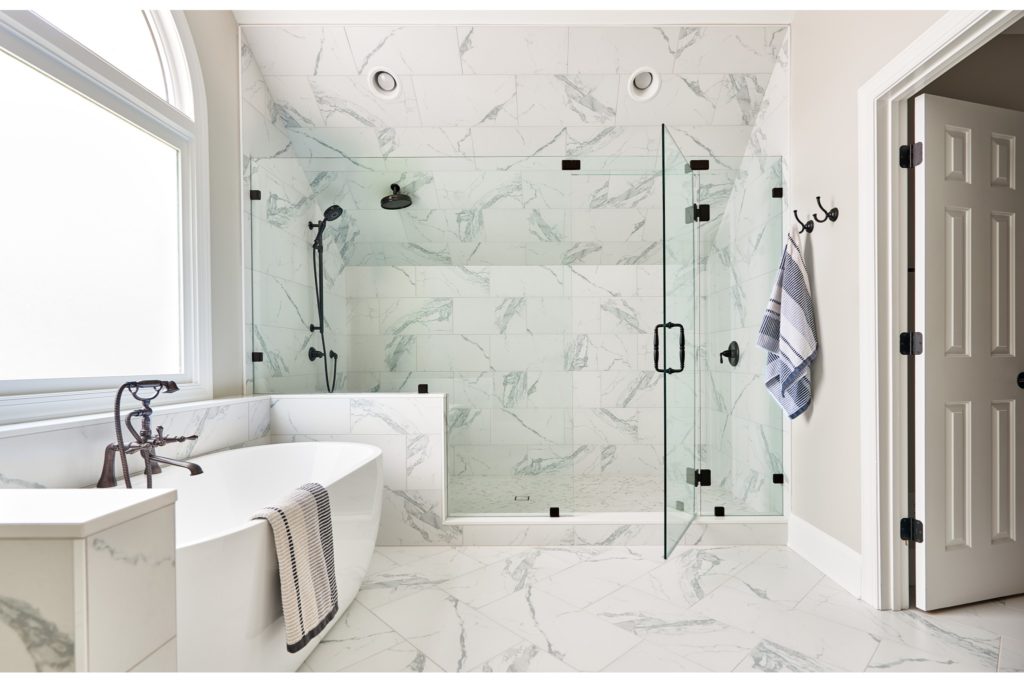 Remodeled bathroom with glass shower and free standing tub. White tile floor and walls, black fixtures.