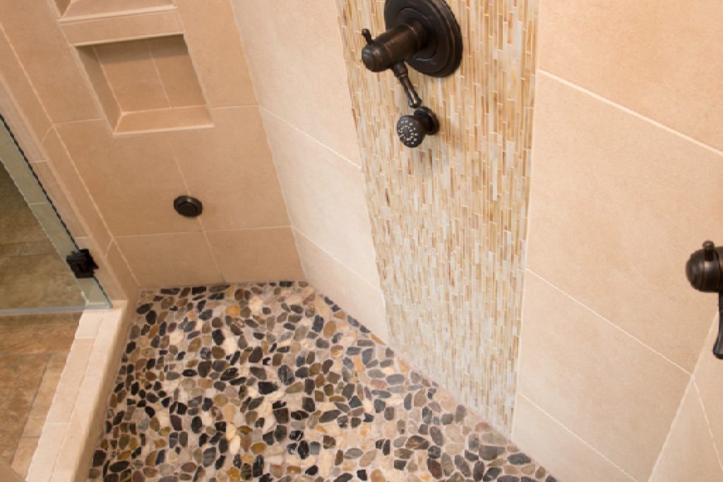 Upgraded custom shower with neutral wall tiles, two stacked niches, and natural pebble-tiled floor