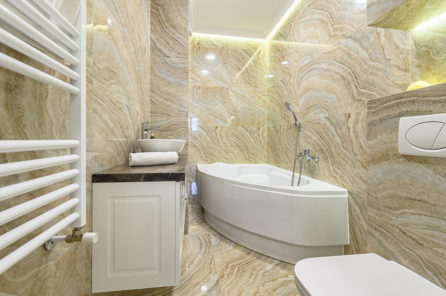 Spacious luxury bathroom with white corner bathtub and beige marble tile floor and walls.
