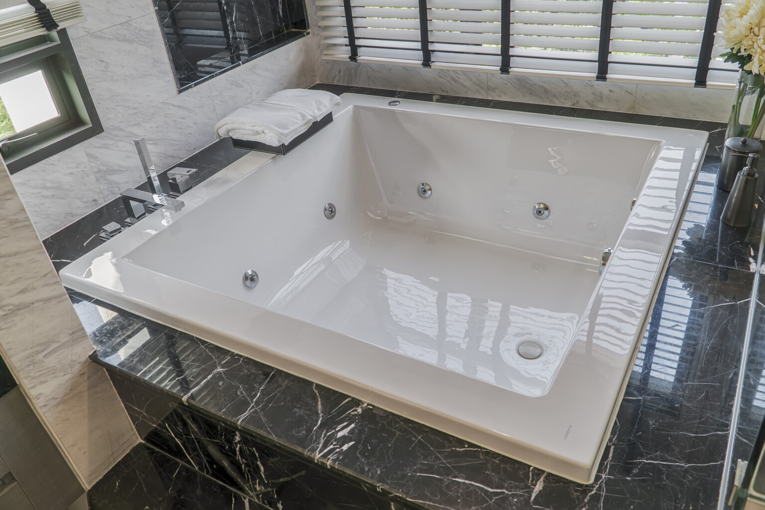 large white square jetted tub in the bathroom, with black marble tile surround.