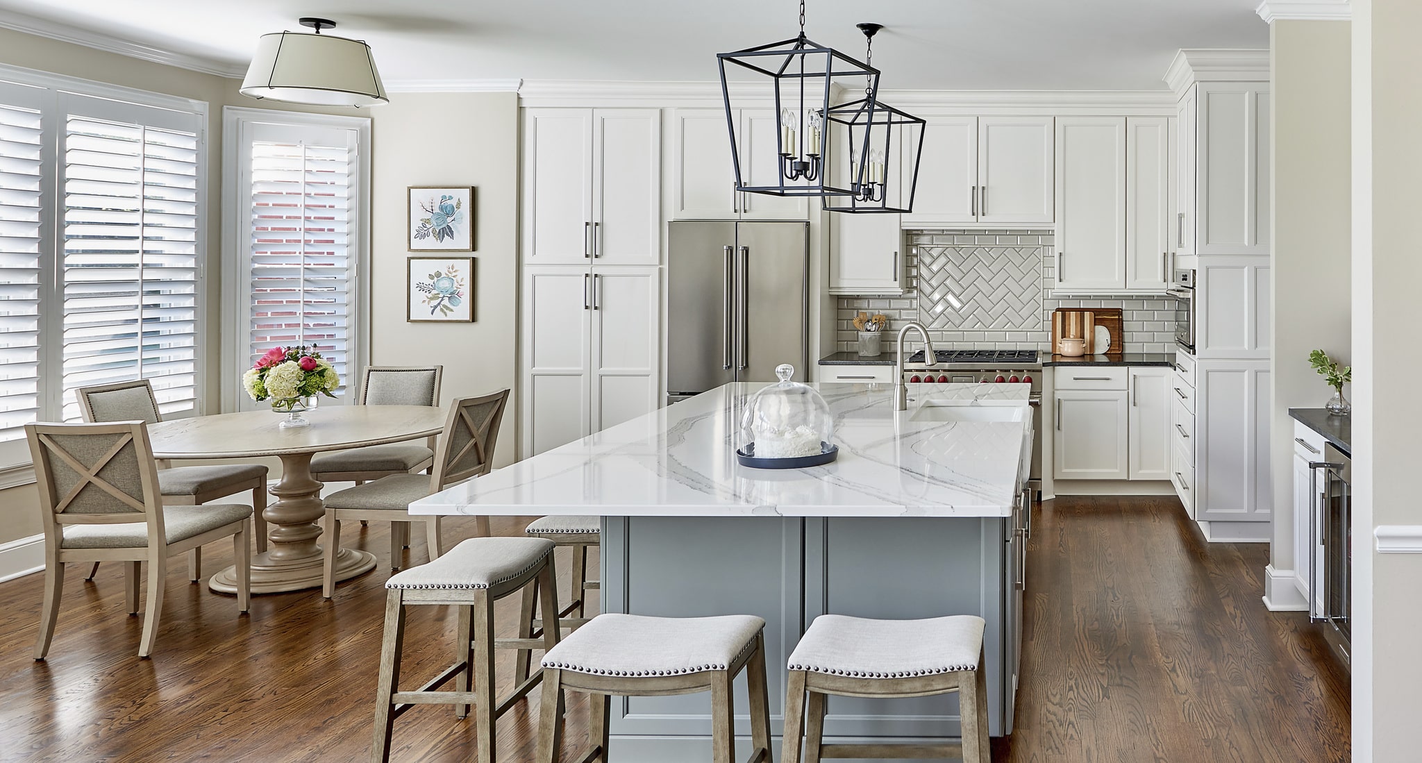 Remodeled kitchen with large island, dining area to the left, pendant lighting, stone countertops, white cabinets, wood floors.