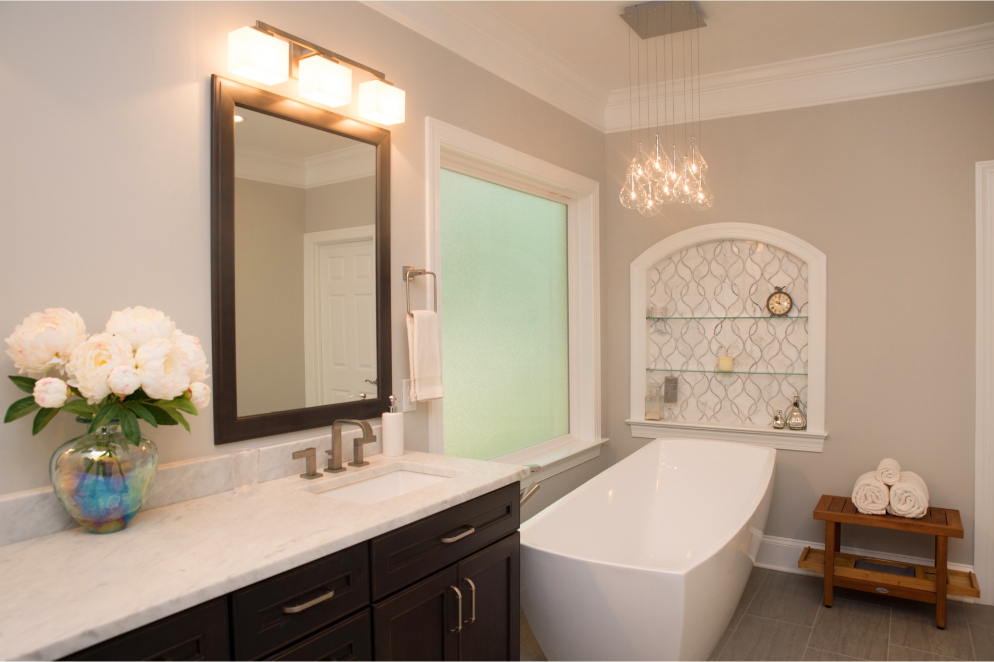 Upgraded bathroom with free-standing tub, large frosted glass window, custom built-in niche, and unique glass bulb chandelier
