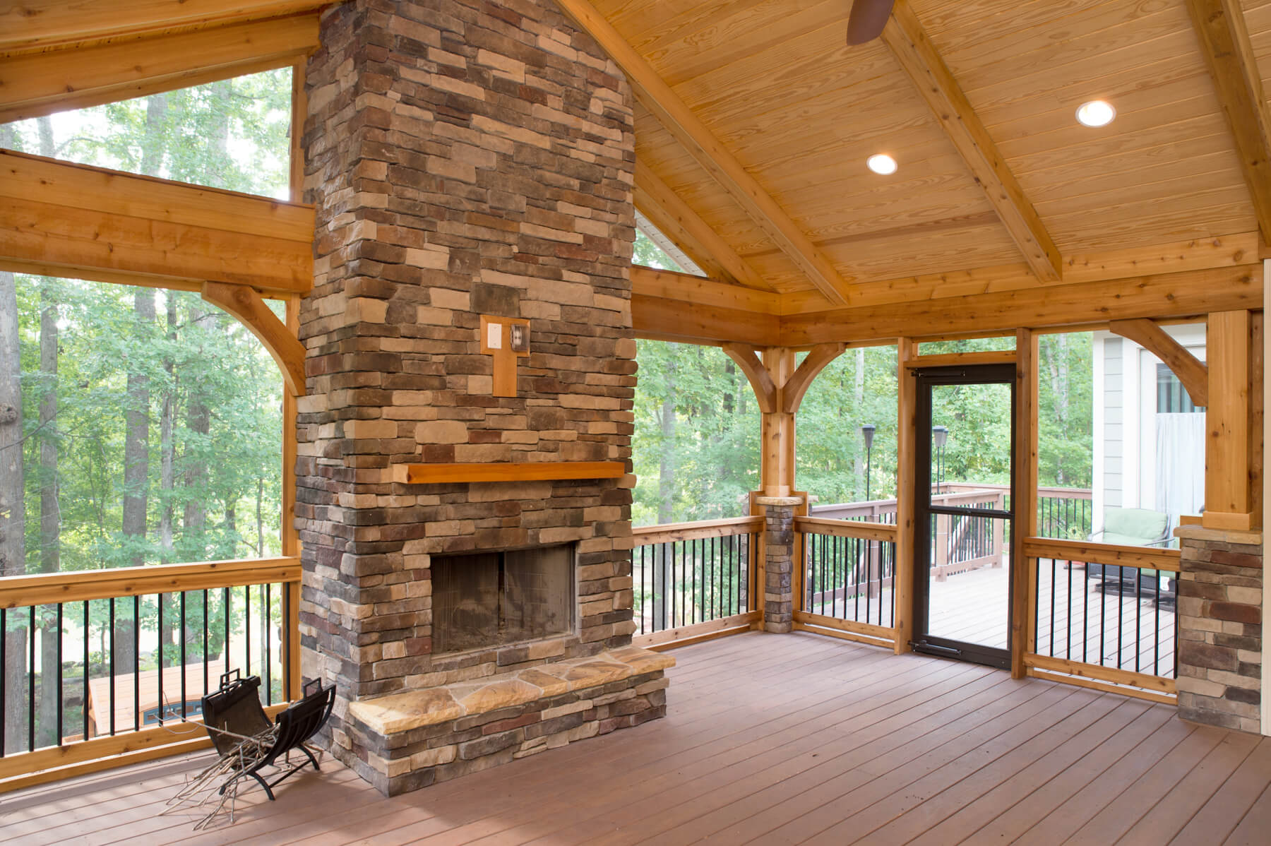Remodeled screened-in porch with large brick fireplace, vaulted wood-beam ceiling, view of forest outside.