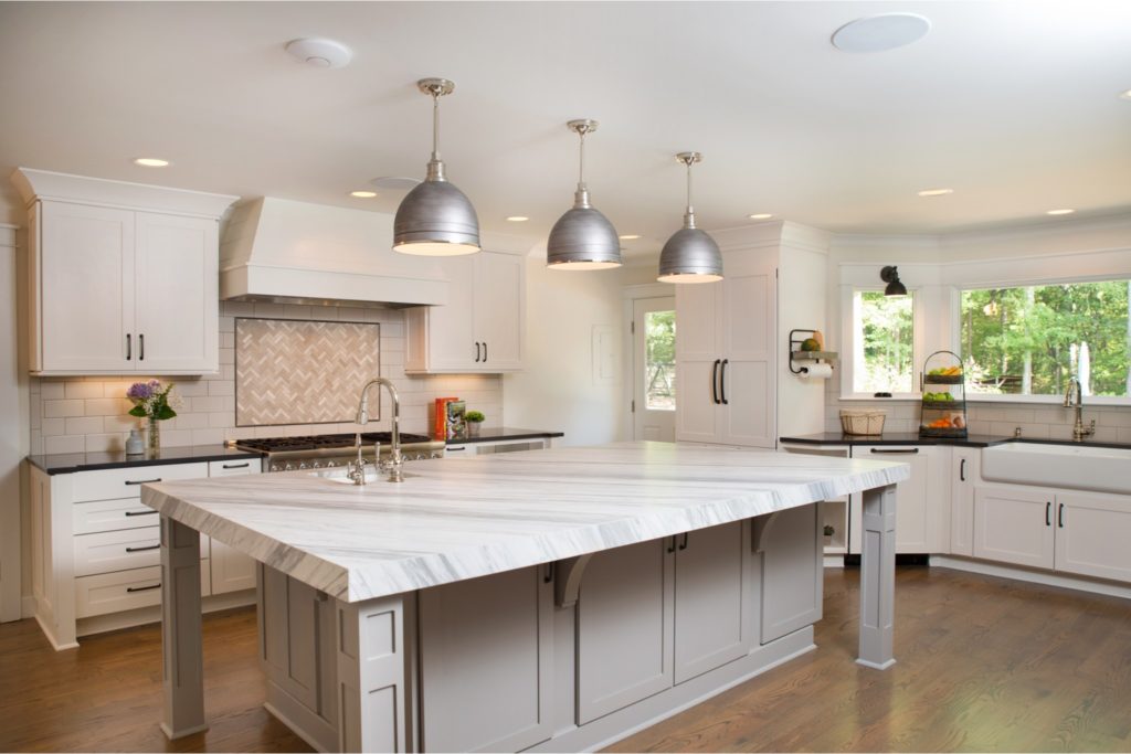 Kitchen renovation with large white granite island with storage, chrome pendant lights, white cabinets, wood flooring