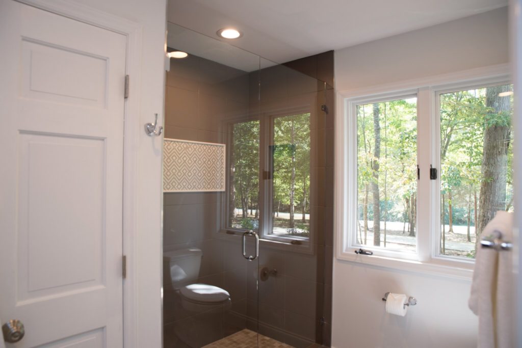 Remodeled bathroom with glass-enclosed shower, white walls, sliding window to the right.
